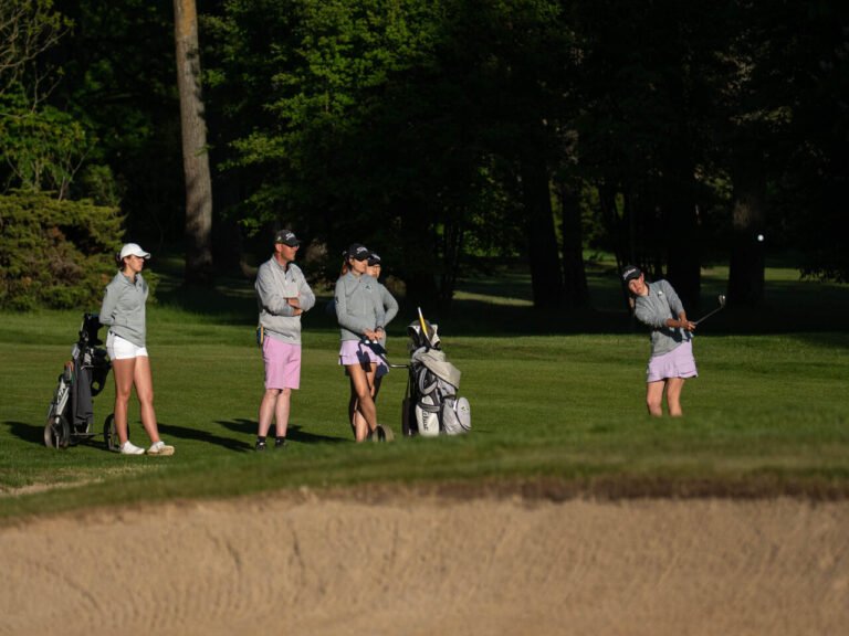 Golf team with coach during training and competition, player hitting a shot near the bunker while teammates watch