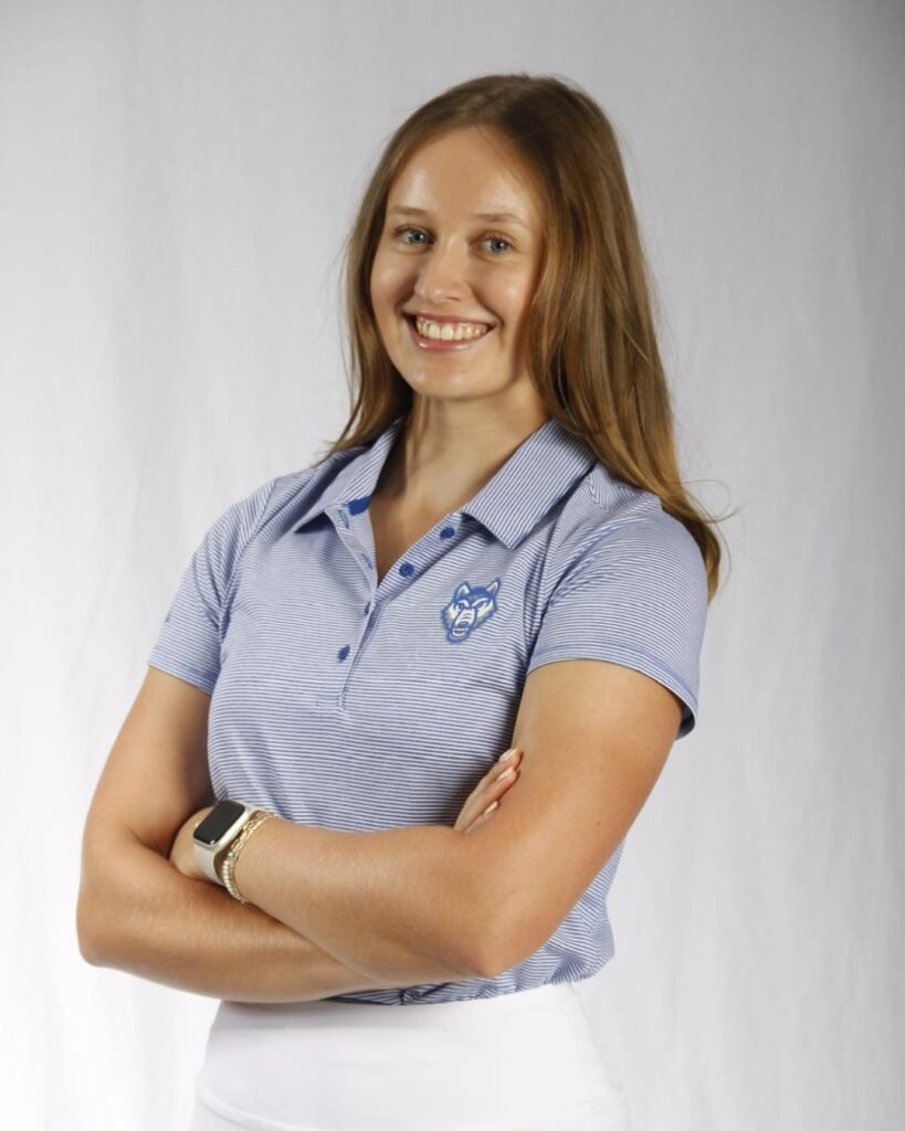 Portrait of Keira Wolf, German golfer, wearing her U.S. college golf team uniform with arms crossed and smiling.