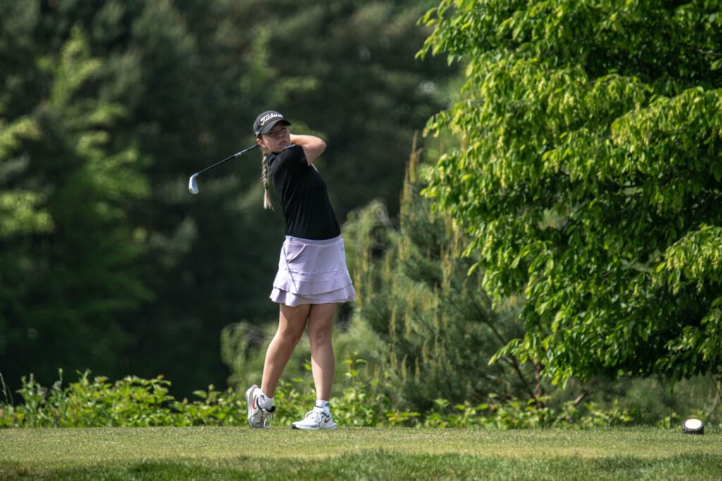 Young female golfer swinging golf club on green course during practice.