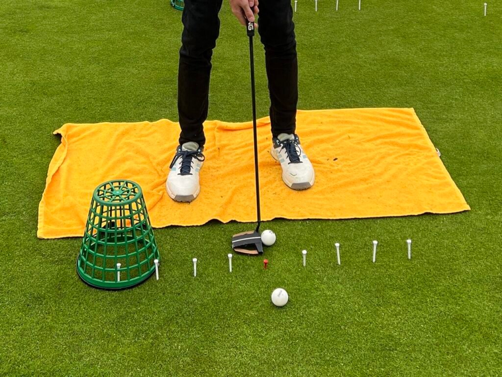 Golf putting drill with tees, basket, towel, and putter for accuracy training.