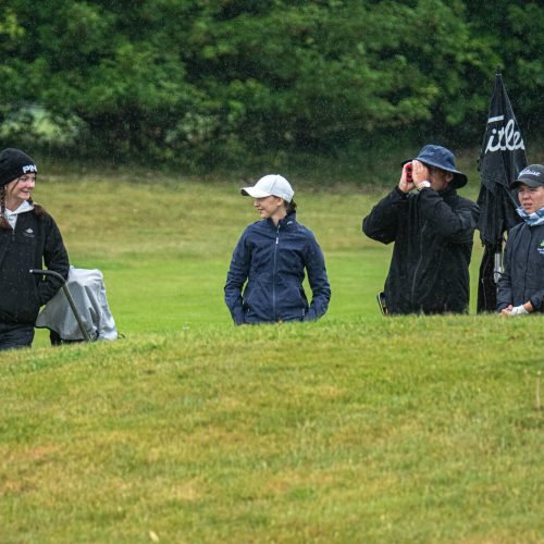 Golf coach and players standing together in rain during tournament round with rangefinder and team discussion